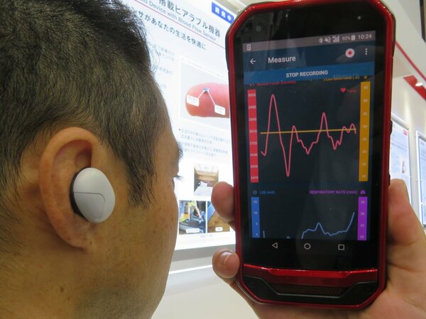 耳に装着して血流量を測定する京セラの新型デバイス。取得データはスマートフォンで表示できる（千葉市・幕張メッセ）