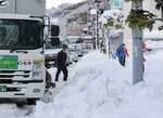 立ち往生するトラックの後ろに伸びる車列と積雪し狭くなった歩道を歩く住民（１２月２７日午後２時７分、彦根市大東町）