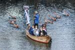 高松城跡の堀で和船に乗り込みトーチを掲げ聖火を運ぶ田野口佳奈さん。後方から約１０人が泳いで続いた＝１８日夕、高松市