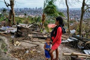 　２５日、息子の隣で、台風で壊れた自宅を見つめる女性＝フィリピン・セブ州（ＡＰ＝共同）