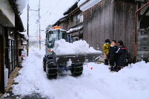 雪遊びする子どもたちと作業に追われる除雪車（２３日午前１０時３４分、宮津市万町）