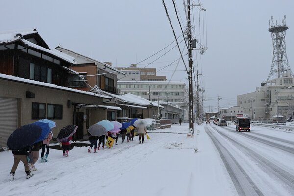降雪の中、傘を差して歩道を進む児童ら。道路は凍結し、車がゆっくり走行していた（１７日午前８時５分、京都府舞鶴市桃山町）