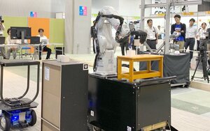正確に部品をつかんむアーム型ロボットの実演に見入る来場者（木津川市・精華町、けいはんなオープンイノベーションセンター）
