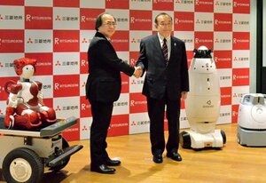 協定締結後に握手する仲谷立命館総長（左）と吉田三菱地所社長。実証実験に用いられるロボットも披露された＝東京都内