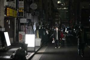 　地震の影響で停電し、明かりが消えた東京・新橋の飲食店街を歩く人たち＝１７日午前０時２１分、東京都港区